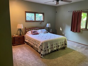 A bedroom with a bed, two bedside tables, a window, and a ceiling fan. - Beautiful Cabin located on the Betsie River and close to Crystal Mountain Resort (Thompsonville)