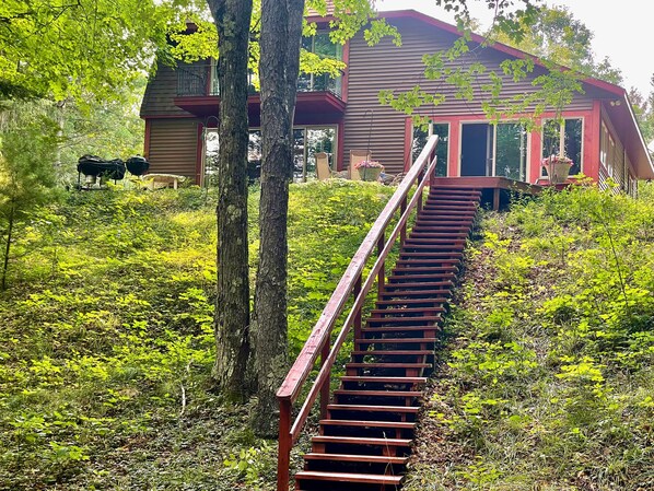 A wooden staircase leading to a house with a red roof, surrounded by lush greenery.