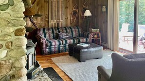 A cozy living room with a stone wall, wooden furniture, and a view of the outdoors. - Beautiful Cabin located on the Betsie River and close to Crystal Mountain Resort (Thompsonville)