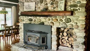 A stone fireplace with a wood-burning stove, a stone wall, and a wooden mantel shelf. - Beautiful Cabin located on the Betsie River and close to Crystal Mountain Resort (Thompsonville)