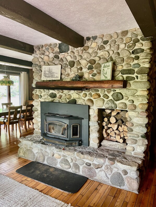 A stone fireplace with a wood-burning stove, a stone wall, and a wooden mantel shelf. - Beautiful Cabin located on the Betsie River and close to Crystal Mountain Resort (Thompsonville)