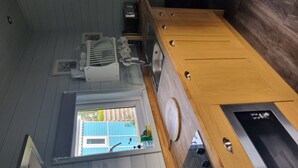 Una cuina amb armaris de fusta, forn integrat i finestra amb vista a una casa blava.