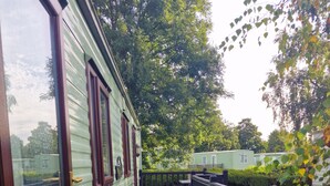 Kapea puinen terassi johtaa vihreään siirtokeloon, jossa on suuret ikkunat ja musta kaide.