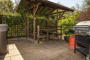 A covered outdoor area with a wooden bench, a barbecue grill, and a gas cylinder. - Secluded, rural retreat nestled in Sherwood Forest, with hot tub (Newark)