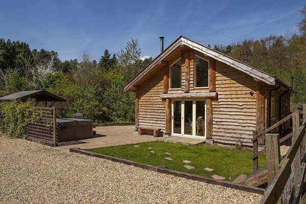 A log cabin with a large sliding glass door, a patio area with a grill, and a fenced garden. - Secluded, rural retreat nestled in Sherwood Forest, with hot tub (Newark)