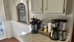 A kitchen with a chalkboard sign, coffee makers, and a window with blinds. - Direct Lakefront Connestee Falls: Views + private dock + 4 kayaks + Not steep! (Brevard)