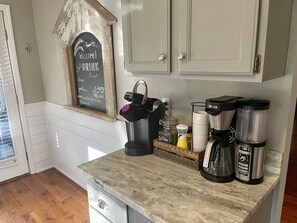 A kitchen with a chalkboard sign, coffee makers, and a window with blinds. - Direct Lakefront Connestee Falls: Views + private dock + 4 kayaks + Not steep! (Brevard)