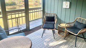 A covered outdoor seating area with wicker chairs and a round table, overlooking a natural landscape. - Direct Lakefront Connestee Falls: Views + private dock + 4 kayaks + Not steep! (Brevard)