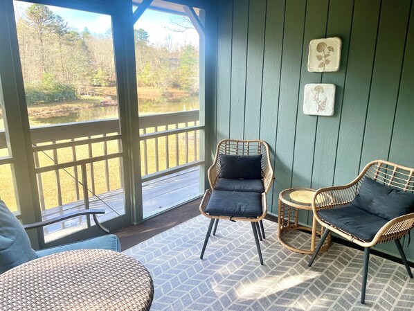 A covered outdoor seating area with wicker chairs and a round table, overlooking a natural landscape.