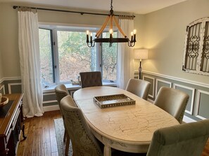 A dining room with a table, chairs, a chandelier, and a view of trees through the window.