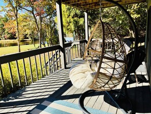 A wooden deck with a wicker swing chair and a bicycle. - Direct Lakefront Connestee Falls: Views + private dock + 4 kayaks + Not steep! (Brevard)