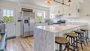 A modern kitchen with white cabinetry, a marble island, and bar stools. - EdiStar at Edisto Beach (Edisto Beach)