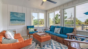 A sunroom with a view of the ocean, featuring a blue sofa, orange armchair, and a wooden coffee table. - EdiStar at Edisto Beach (Edisto Beach)