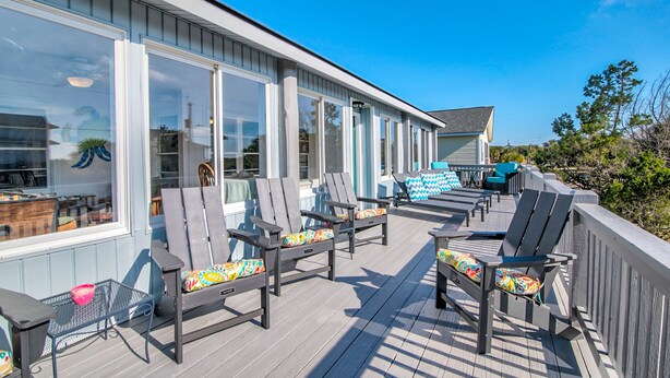 A covered outdoor deck with grey Adirondack chairs and a table, overlooking a body of water. - EdiStar at Edisto Beach (Edisto Beach)