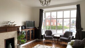 A living room with a fireplace, a television, two armchairs, a sofa, and a large window with a view of buildings.