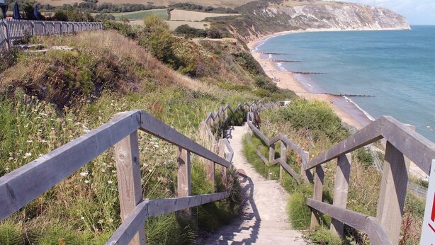 A wooden staircase leading to a beach with a view of cliffs and the sea.
