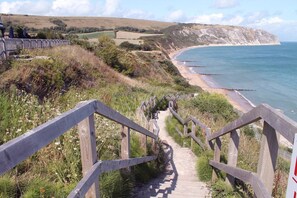 Eine Holztreppe führt zu einem Strand mit Blick auf Klippen und das Meer.