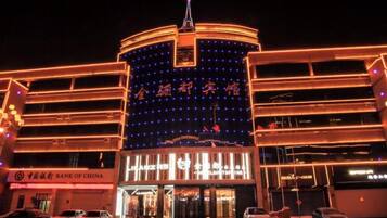 A multi-story building with illuminated signage and a prominent entrance, surrounded by parked cars.