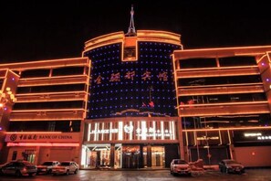 A multi-story building with illuminated signage and a prominent entrance, surrounded by parked cars. - Jinlidu Hotel (Tieli)
