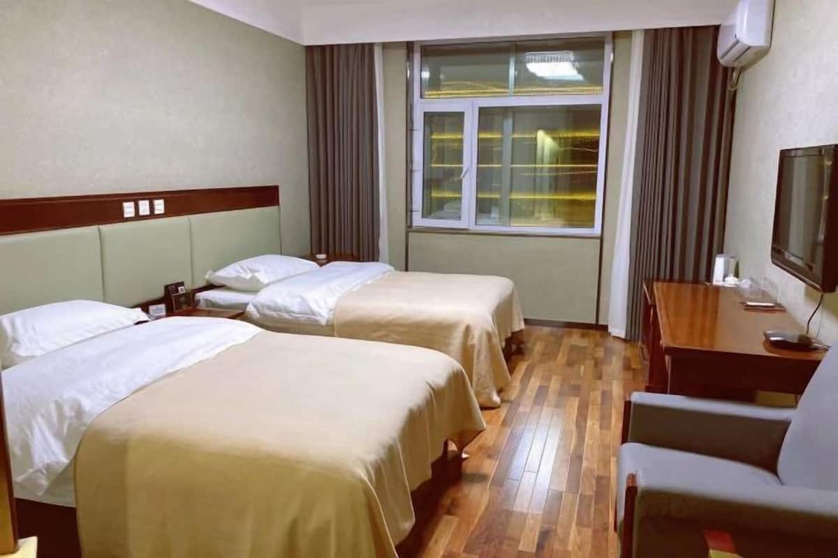 Habitación de hotel con dos camas individuales, piso de madera, un escritorio con silla y un televisor.