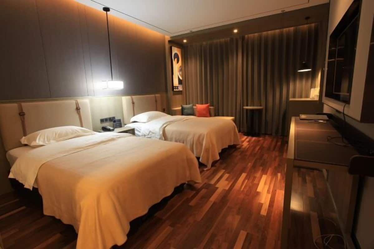 Una habitación de hotel con dos camas, un escritorio, un televisor y una ventana con cortinas.