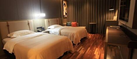 A hotel room with two beds, a desk, a TV, and a window with curtains.