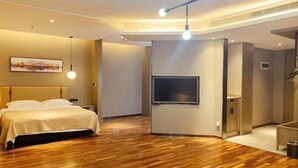Una habitación de hotel moderna con suelo de madera, una cama con ropa de cama blanca, un televisor de pantalla plana montado en la pared y una lámpara en el techo.