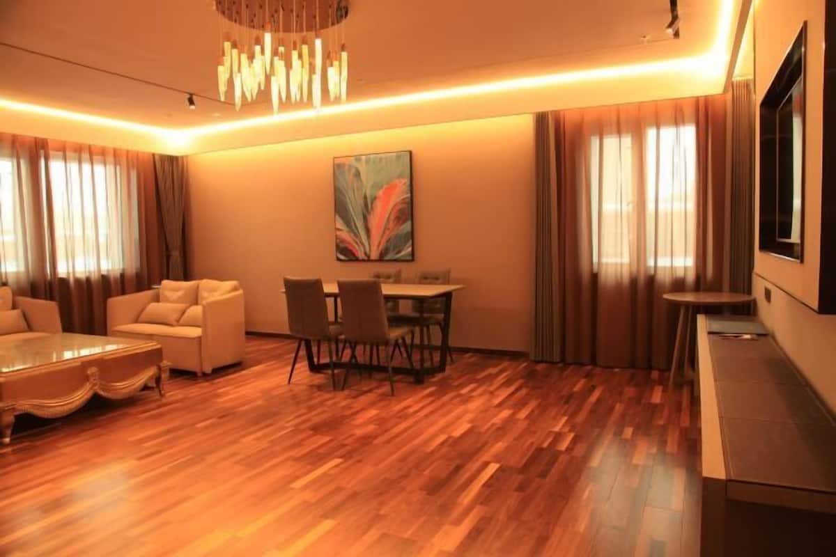 Una sala de estar moderna con piso de madera, una mesa de comedor con sillas, un sofá, una mesa de centro y un televisor a la derecha.