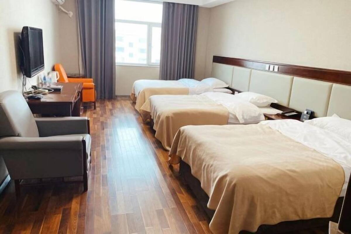Habitación de hotel con tres camas, un escritorio, una silla y un televisor.