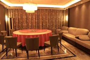 A round table with a red tablecloth surrounded by chairs, a sofa, and a patterned curtain backdrop. - Jinlidu Hotel (Tieli)