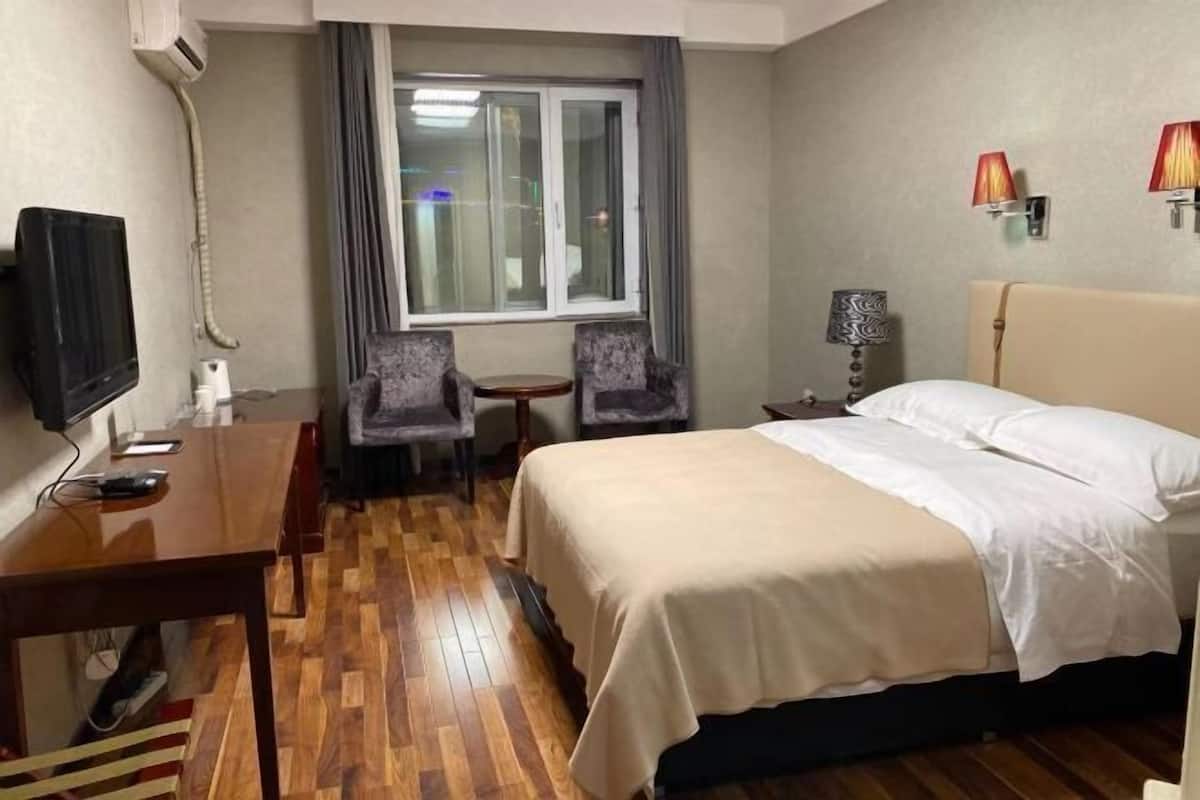 Una habitación de hotel con cama, escritorio, silla, televisor y ventana con cortinas.