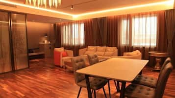 A modern living room with a wooden floor, a sofa set, a dining table, and a large window with curtains.