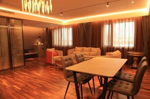 Una sala de estar moderna con suelo de madera, un conjunto de sofás, una mesa de comedor y un amplio ventanal con cortinas.