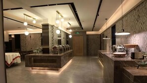 Un lobby moderno de hotel con un mostrador de recepción de mármol, iluminación colgante, un área de descanso con mesas y una pared con diseño.