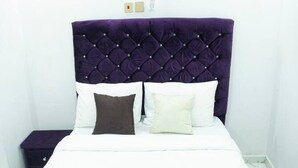 A bed with a tufted headboard, white bedding, and two bedside tables. - Charming 1-bed Apartment in Abuja (Abuja)