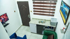 A compact kitchen with a sink, a small refrigerator, and a window with blinds. There is a blue chair and a green sofa in the living area. - Charming 1-bed Apartment in Abuja (Abuja)