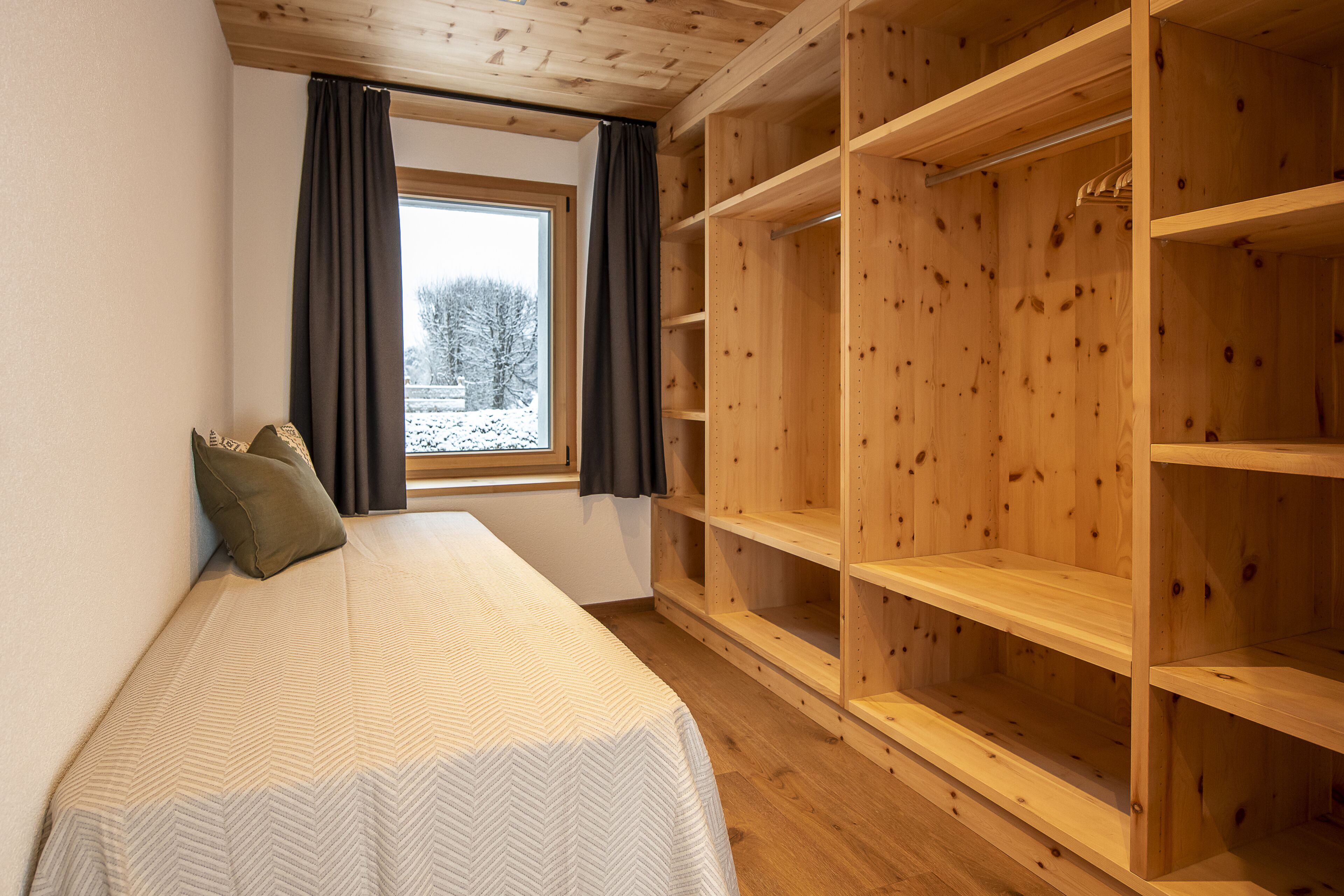 A bedroom with a bed, a window with curtains, and a wooden wardrobe.