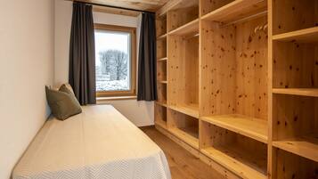 A bedroom with a bed, a window with curtains, and a wooden wardrobe.