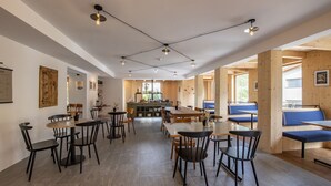 A spacious dining area with multiple tables and chairs, wooden beams on the ceiling, and a kitchen in the background.
