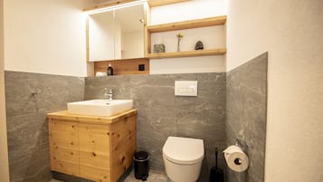 Un baño moderno con tocador de madera, un lavabo blanco, un inodoro y un estante sobre el tocador.