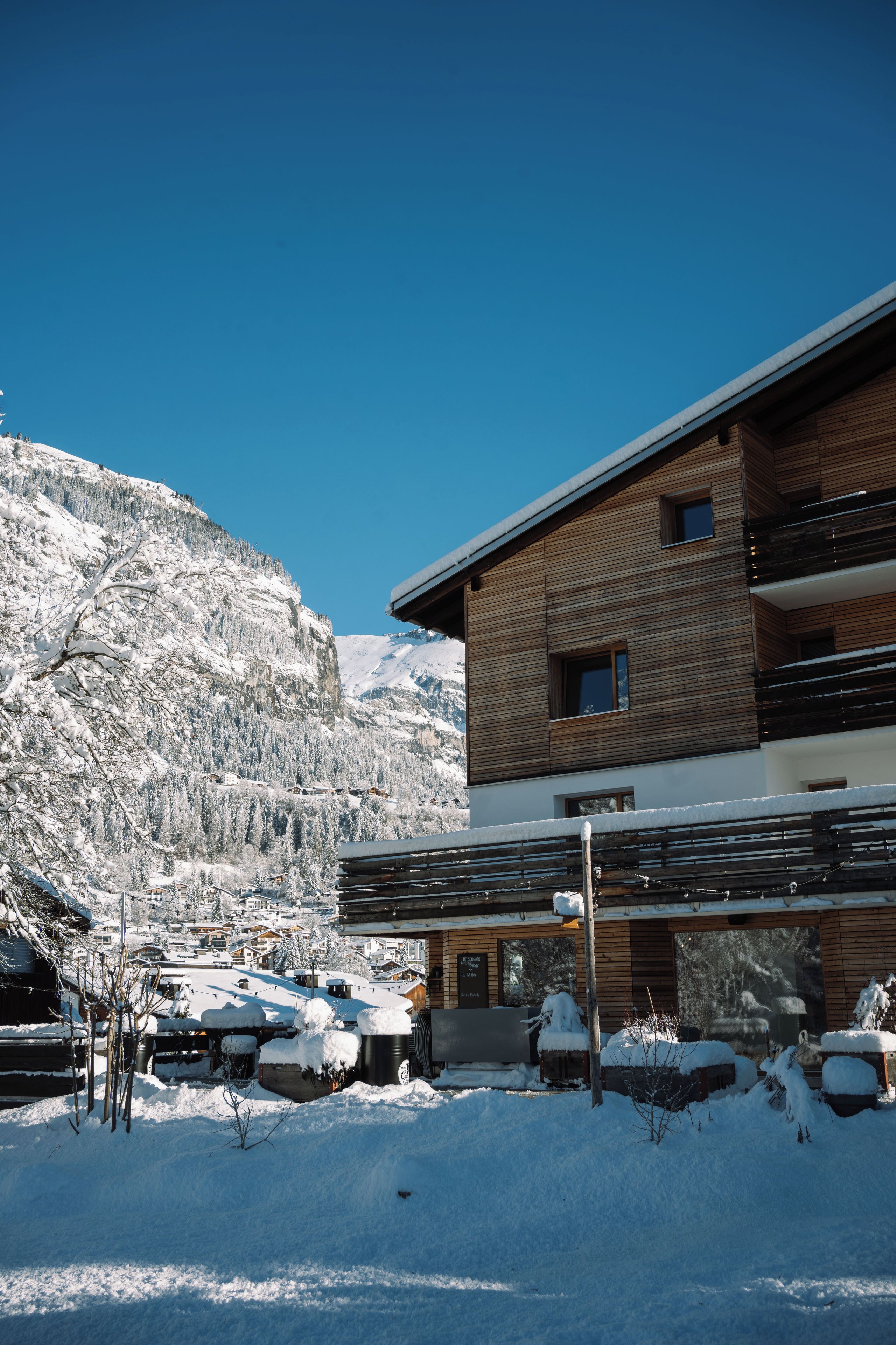 A modern building with a wooden facade, a balcony, and a view of snow-covered mountains.