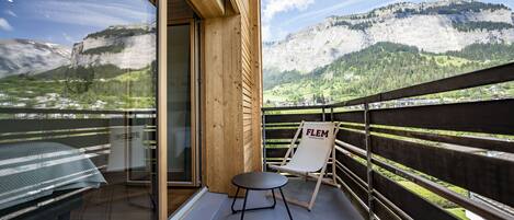 A balcony with a glass door, a small round table, a folding chair, and a view of mountains.