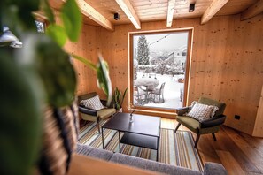 A cozy room with wooden walls, a large window, a sofa, two armchairs, and a small table. - Flem Mountain Lodge (Flims)