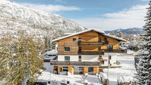 A multi-story wooden chalet with a balcony, surrounded by snow-covered trees and mountains. - Flem Mountain Lodge (Flims)