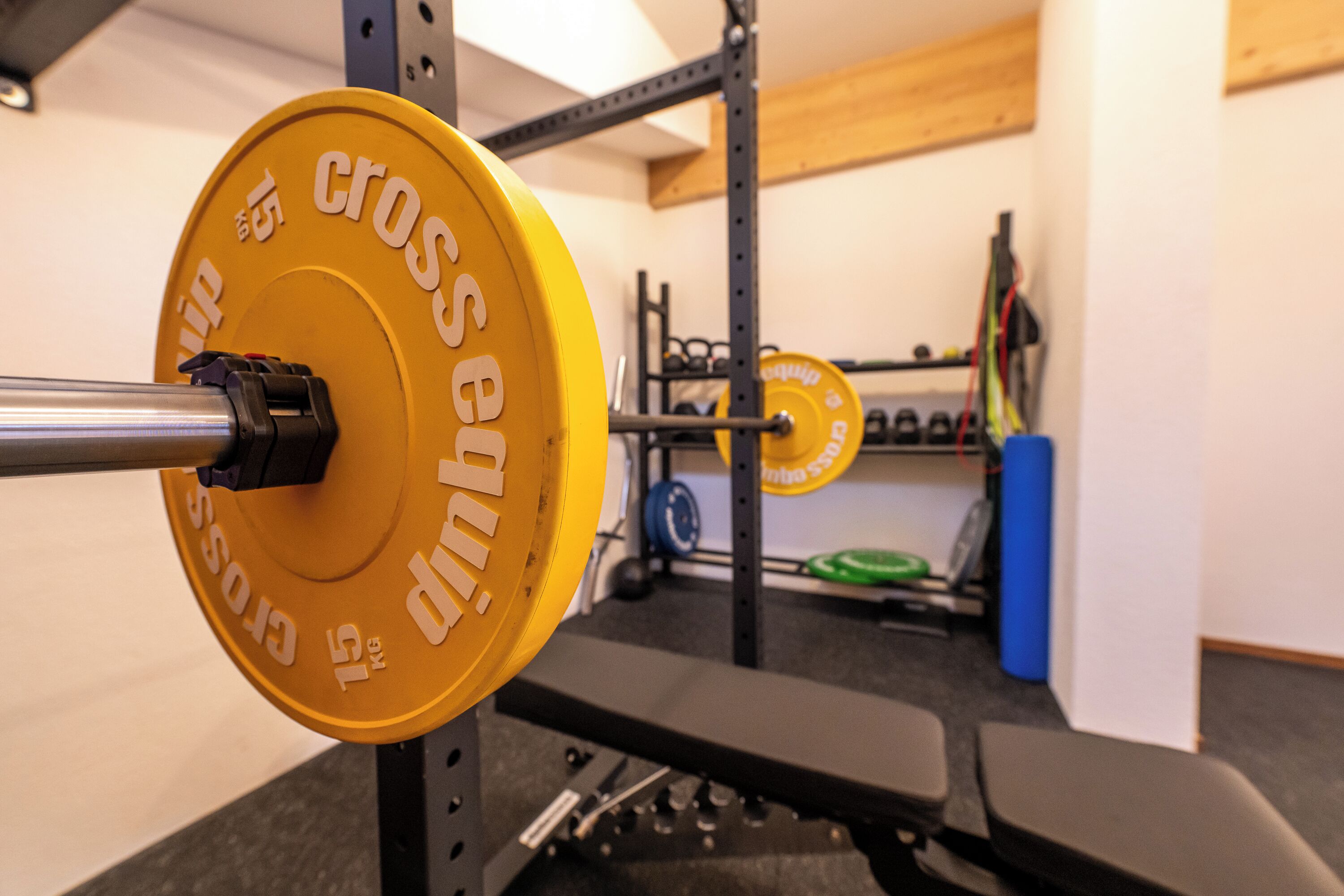 A weightlifting bench with a barbell and a yellow weight plate labeled 'cross' in a gym setting.