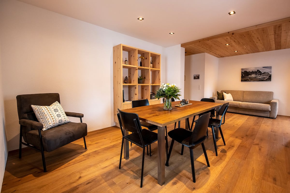 A modern dining area with a wooden table, black chairs, and a built-in wooden shelving unit.