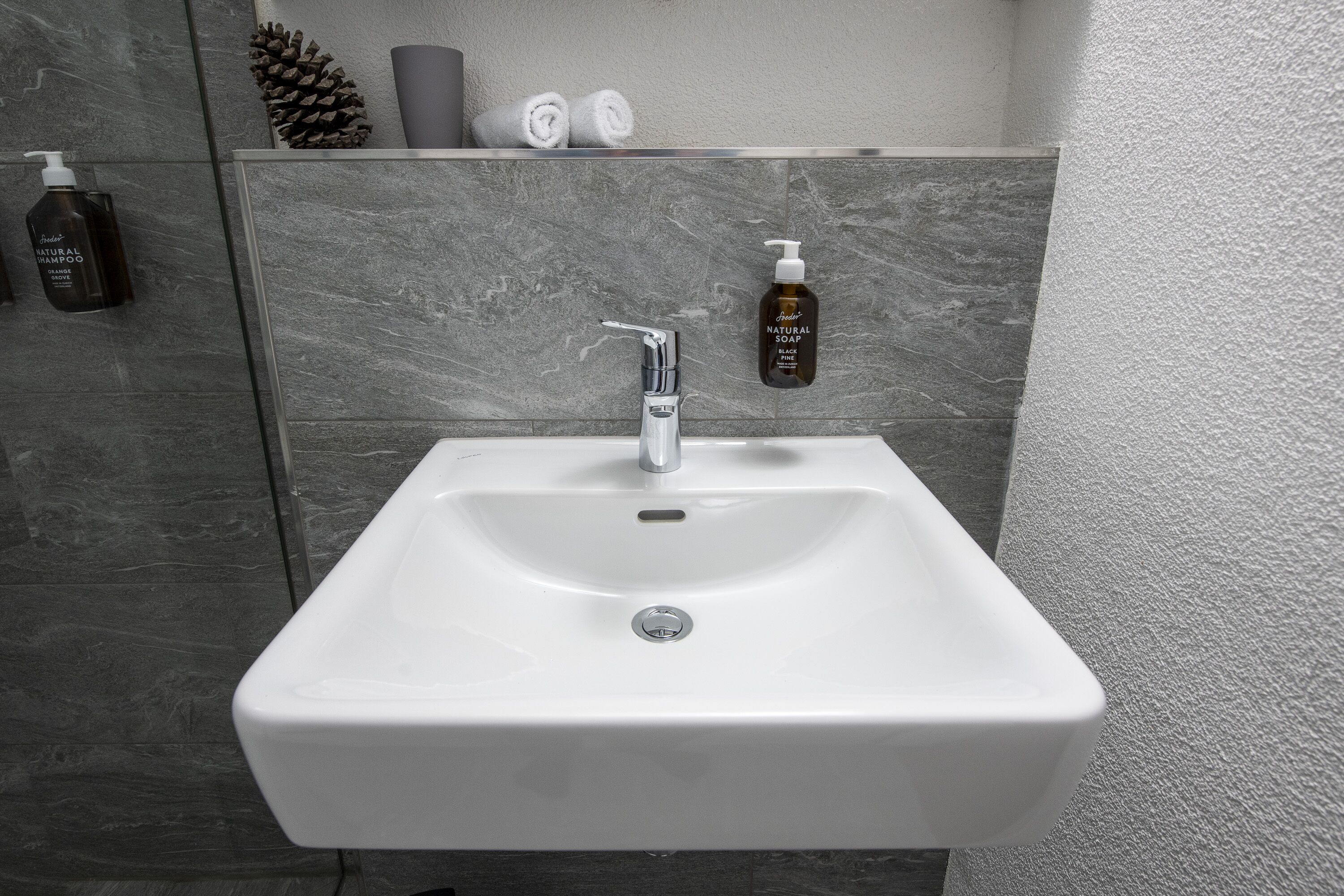 Een badkamer met een wit wastafelmeubel, een moderne kraan en twee zeepflessen aan de muur.