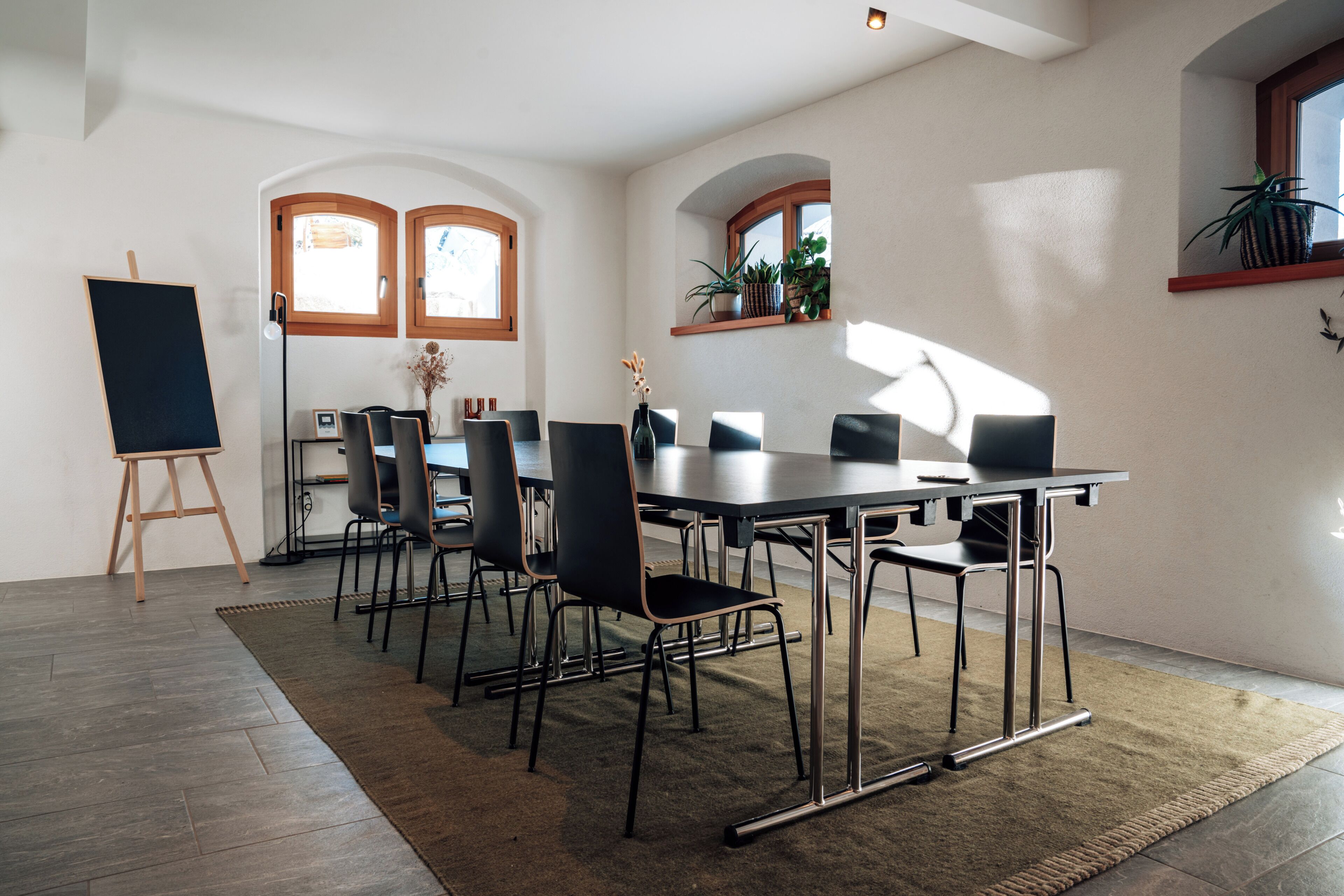 A conference room with a long table, multiple chairs, a standing easel, and potted plants.