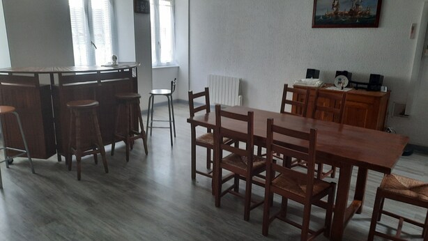 A spacious dining area with a wooden table and chairs, a kitchen area with a bar, and large windows providing natural light. - beautiful apartment 150m2, 4 bedrooms, 6 people (Noidans-le-Ferroux)