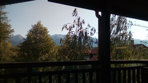 A view from a covered balcony with a mountain backdrop, trees, and a building with a red roof.